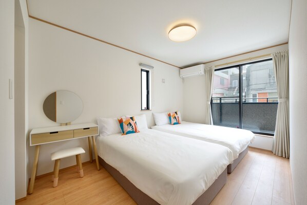 Une chambre avec deux lits, un bureau, une chaise, une fenêtre avec des rideaux et un appareil de climatisation.