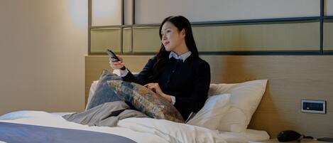 Een hotelkamer met een bed, een nachtkastje met een lamp en een bedieningspaneel aan de muur.