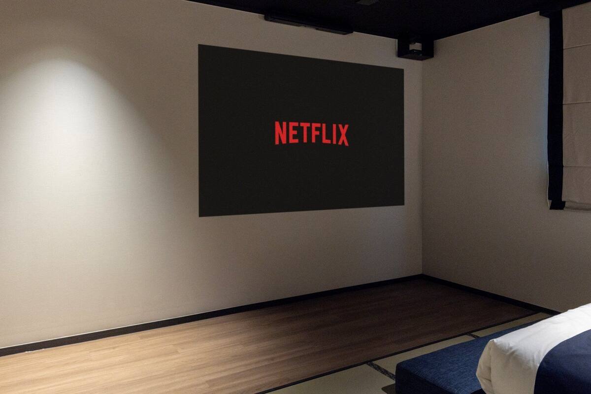 Habitación con cama, una pantalla mural que muestra 'NETFLIX' y una ventana con persiana.