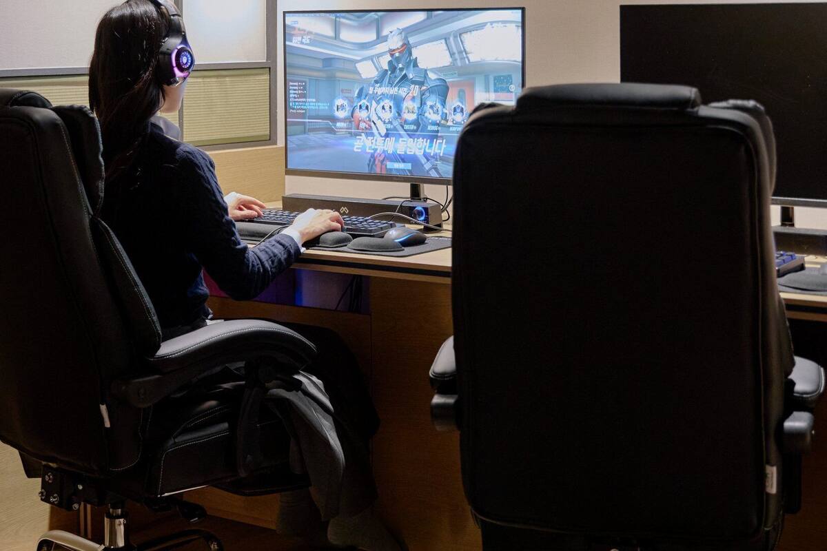 Una persona usando un visor de realidad virtual en un escritorio con un monitor de computadora mostrando un juego, en una oficina con una silla y un teclado.