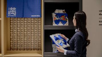 A person examining a fabric with a blue ribbon in a display case with a grid pattern and a blue banner with text.