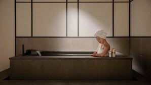 Una persona en una bañera con una toalla en la cabeza, una botella y una lata en el borde.