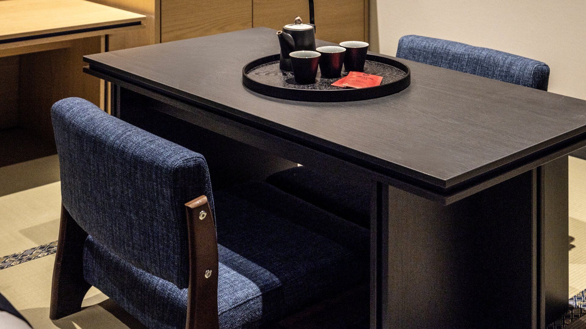 Une table à manger avec un plateau noir, quatre chaises et un plateau contenant une théière et des tasses.