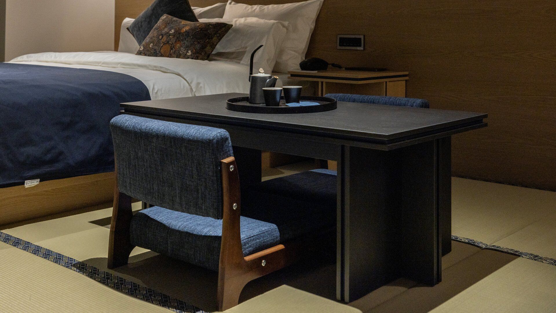 A hotel room with a bed, a small table with chairs, and a nightstand.