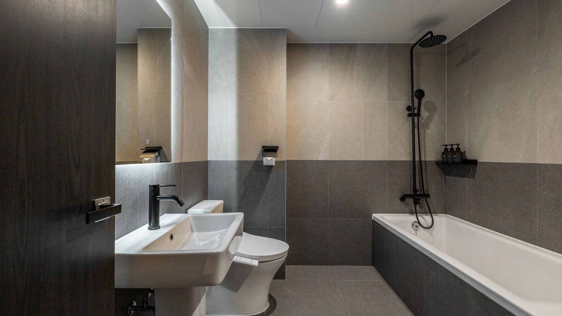 A modern bathroom with a toilet, sink, and bathtub, featuring a minimalist design and neutral color palette.