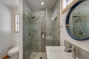 Ein modernes Badezimmer mit einer gläsernen Duschkabine, einer weißen Toilette, einem Waschbecken mit Spiegel und einer gefliesten Duschwand.