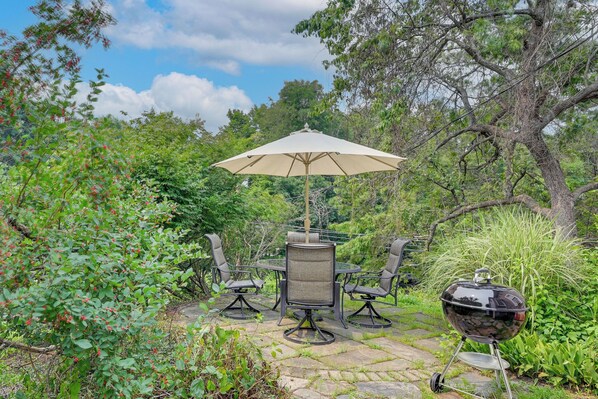 Une terrasse extérieure avec une table et des chaises, un parasol et un barbecue.