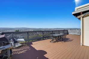 A wooden deck with a table and chairs, a grill, and a view of the cityscape. - Bay Area Family Home w/ Indoor Pool + Game Room (South San Francisco)