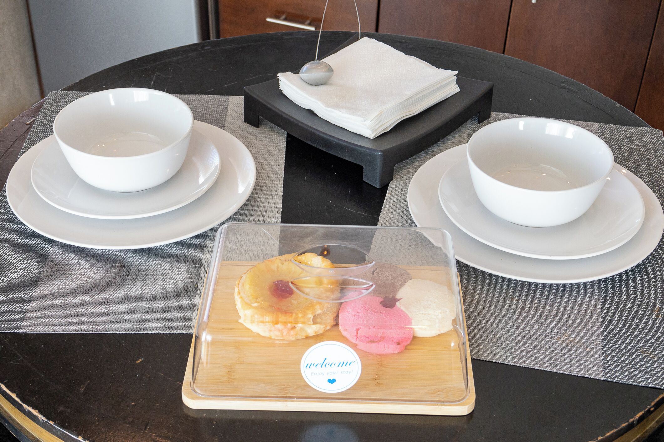 A round table with two white bowls and a clear plastic container with pastries.