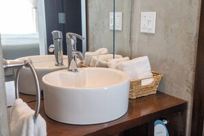 A bathroom with a large white sink, two faucets, a mirror, and a wicker basket with towels.
