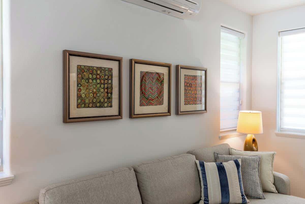 Ein Wohnzimmer mit einer Couch, drei gerahmten Kunstwerken an der Wand und einer Lampe.