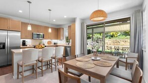 A modern kitchen with wooden cabinets, stainless steel appliances, and a dining area with a table and chairs. - @ Marbella Lane Hale Lai Serene Luxury 3BR Home (Waianae)