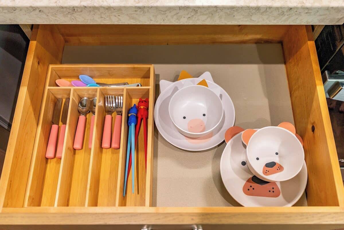 A drawer with utensils, plates, and a bear-shaped bowl.