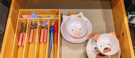 A drawer with utensils, plates, and a bear-shaped bowl.