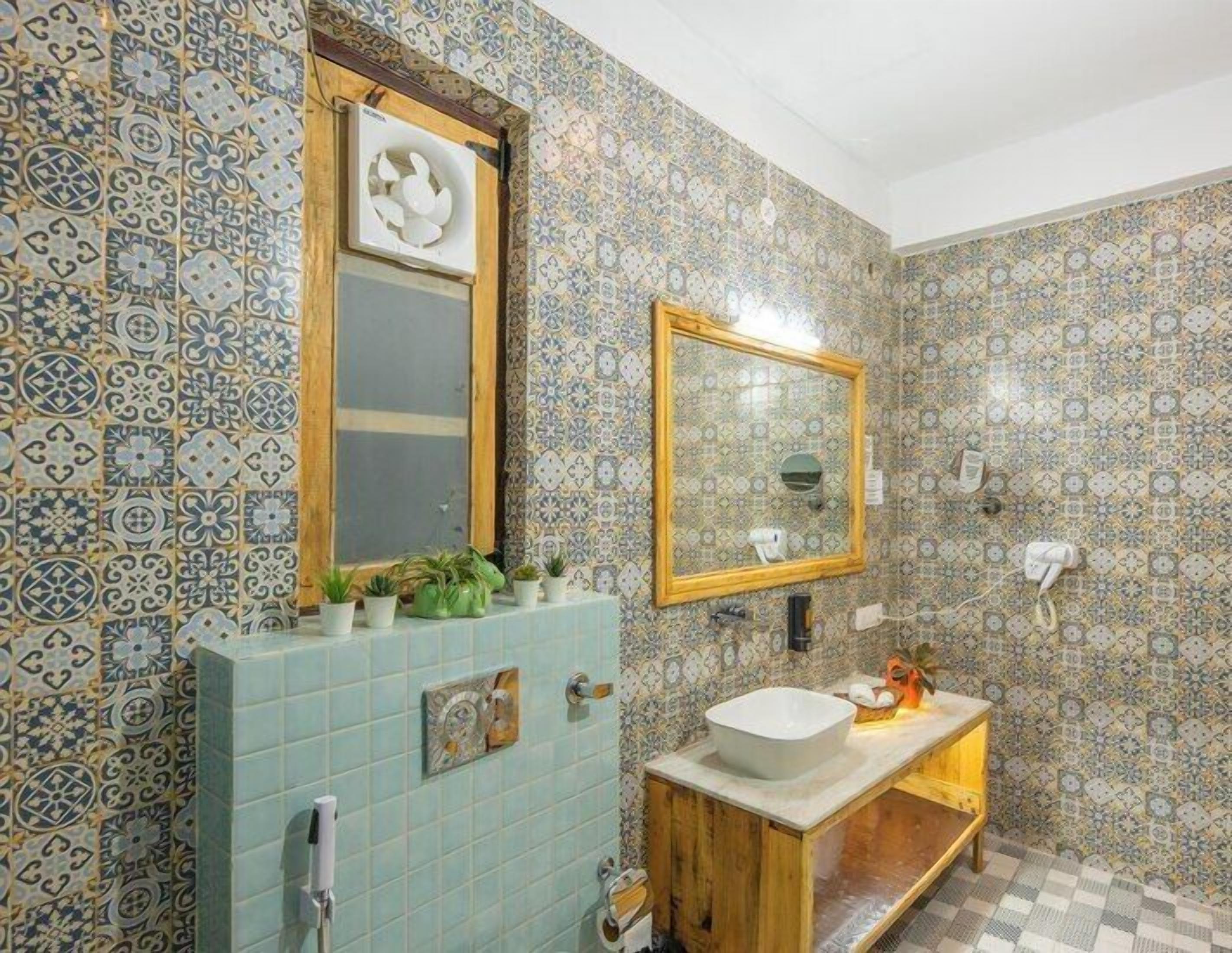 A bathroom with patterned tiles, a wooden vanity, a sink, a mirror, and a small shelf with plants.