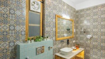 A bathroom with patterned tiles, a wooden vanity, a sink, a mirror, and a small shelf with plants.