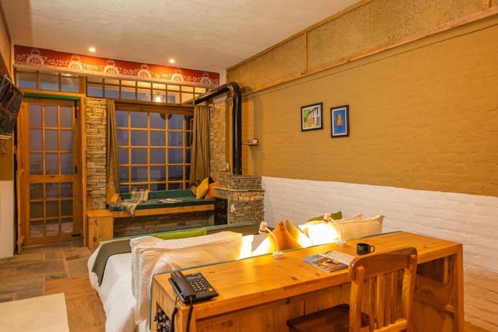 Una habitación acogedora con chimenea de piedra, un escritorio de madera y una cama con vistas al exterior.
