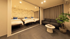 Une chambre d’hôtel avec un mur recouvert de miroirs, trois lits, un canapé, une table basse et une plante en pot.