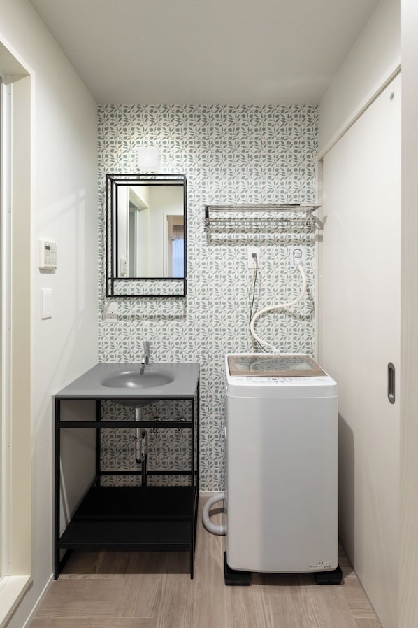 Un baño pequeño con lavamanos, espejo, toallero y una lavadora blanca.