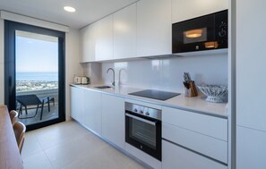 Eine moderne Küche mit Einbauofen, Spüle und Mikrowelle. Durch das Fenster ist der Meerblick zu sehen.