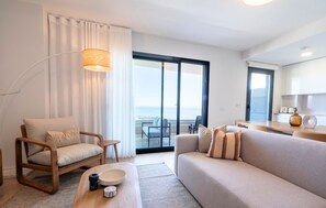 A modern living room with a sofa, armchair, and a coffee table. There is a large window with a view of the sea. - Bali Vista Contemporary Three-Bedroom Apartment with Pool & Gym close to Malaga (Rincón de la Victoria)