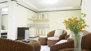 Una habitación con mobiliario de mimbre, una zona de cocina y un jarrón con flores.