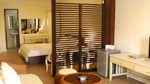 Habitación de hotel con cama, escritorio, refrigerador, mobiliario de mimbre y un separador.