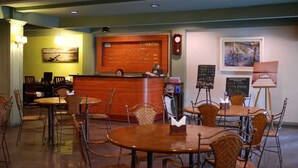 Un restaurante con barra de madera, varias mesas y sillas, un tablero de menú y obras de arte en las paredes.