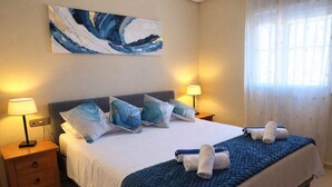 Une chambre d’hôtel avec un lit, deux lampes de chevet, une table de nuit, une couverture bleue et un tableau au mur.