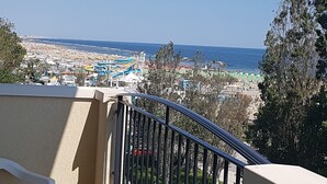Un balcón con vista a la ciudad costera, que incluye una playa y un parque acuático.