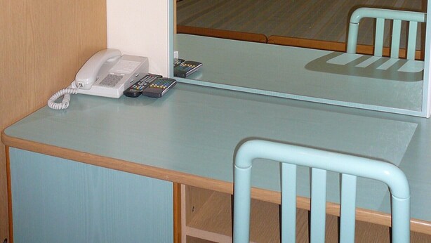 Una habitación con una cama, un escritorio con teléfono y controles remotos, una silla y un espejo.