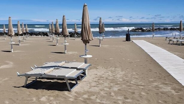 A beach with rows of sun loungers and umbrellas, a concrete walkway, and the ocean in the background. - Hotel de la Plage (Rimini)