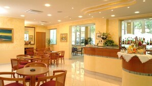 A hotel lobby with round tables and chairs, a reception desk, and a bar area. - Hotel de la Plage (Rimini)