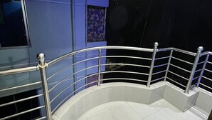 Un balcon incurvé avec des balustrades en métal, un sol carrelé et un mur orné d’un motif bleu et noir.
