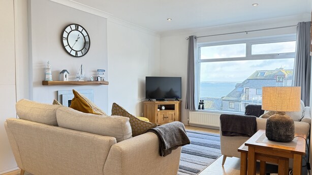 A modern living room with a sofa, television, and a view of the sea. - Clearwater Seaview a perfect retreat (St Ives)