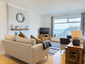 A modern living room with a sofa, television, and a view of the sea. - Clearwater Seaview a perfect retreat (St Ives)