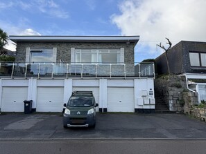 Ein modernes, zweistöckiges Haus mit Naturstein-Fassade, einem Balkon mit Glasgeländern und einem parkenden Auto davor.