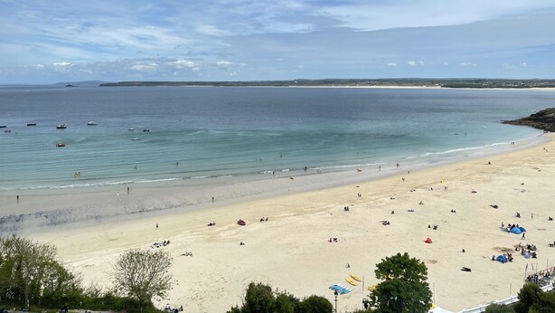 Uma praia com céu claro, águas calmas e areal arenoso.