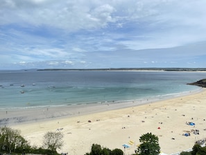 Ein Strand mit blauem Himmel, ruhigem Wasser und sandigem Ufer.