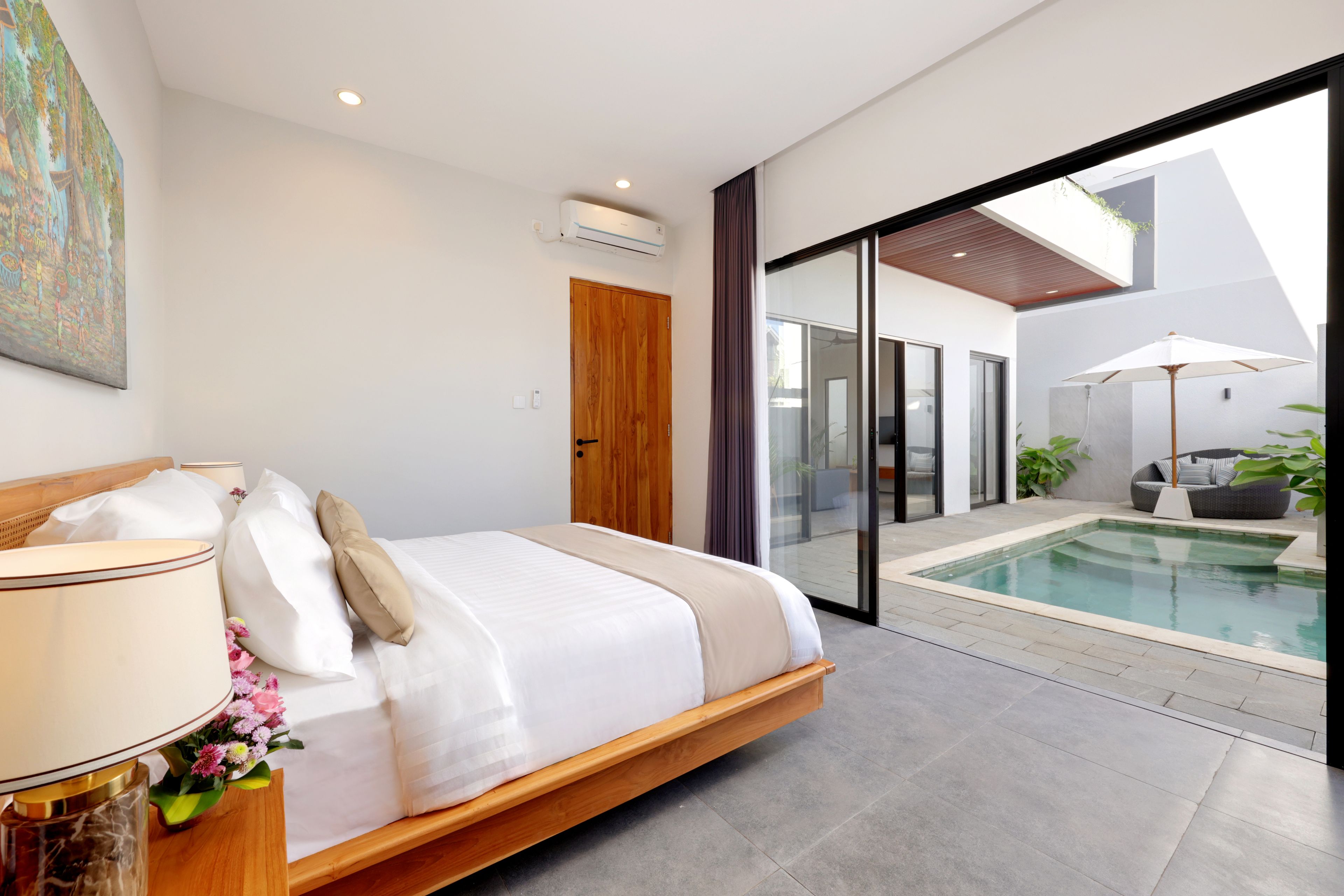 Ein modernes Schlafzimmer mit einem großen Bett, einer Nachttischlampe und Blick auf einen Swimmingpool.