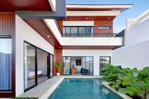 Uma casa moderna de dois andares, com piscina, janelas amplas e varanda.