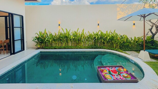 Una piscina con una plataforma flotante en el centro, rodeada de exuberante vegetación y un cielo despejado.