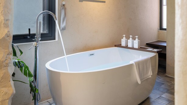Ein modernes Badezimmer mit einer freistehenden Badewanne, einer Wandleuchte und einem Fenster für natürliches Licht.