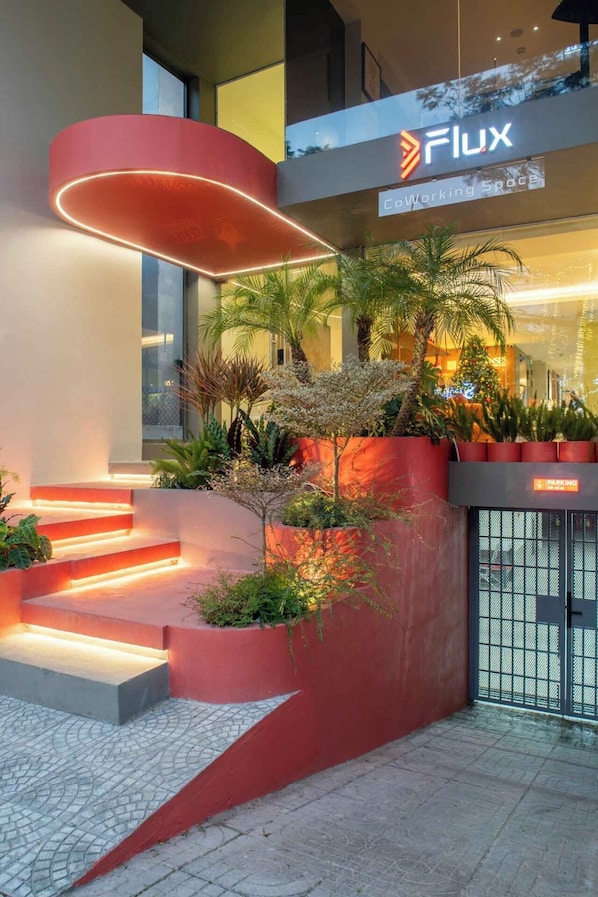 Una entrada de edificio moderno con una estructura roja, plantas exteriores y un letrero que dice 'Flux Working Space'.