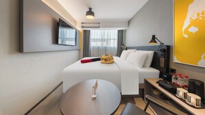 Une chambre d’hôtel moderne, équipée d’un lit, d’une table de chevet, d’une lampe et d’une carte accrochée au mur.