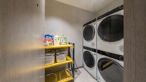 Une buanderie équipée d’un lave-linge et d’un sèche-linge, d’étagères pour ranger les produits de nettoyage et de bacs de rangement.