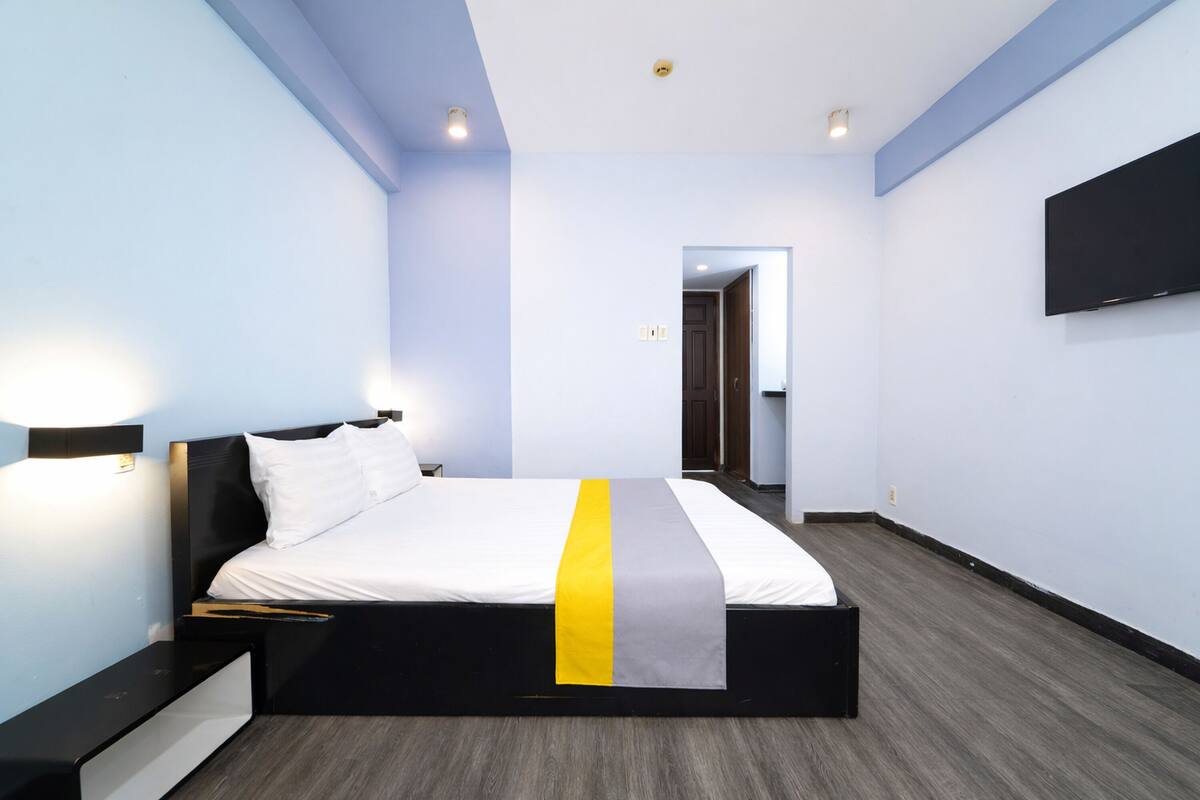 A modern hotel room with a bed, bedside tables, a flat-screen TV, and a door leading to another room.