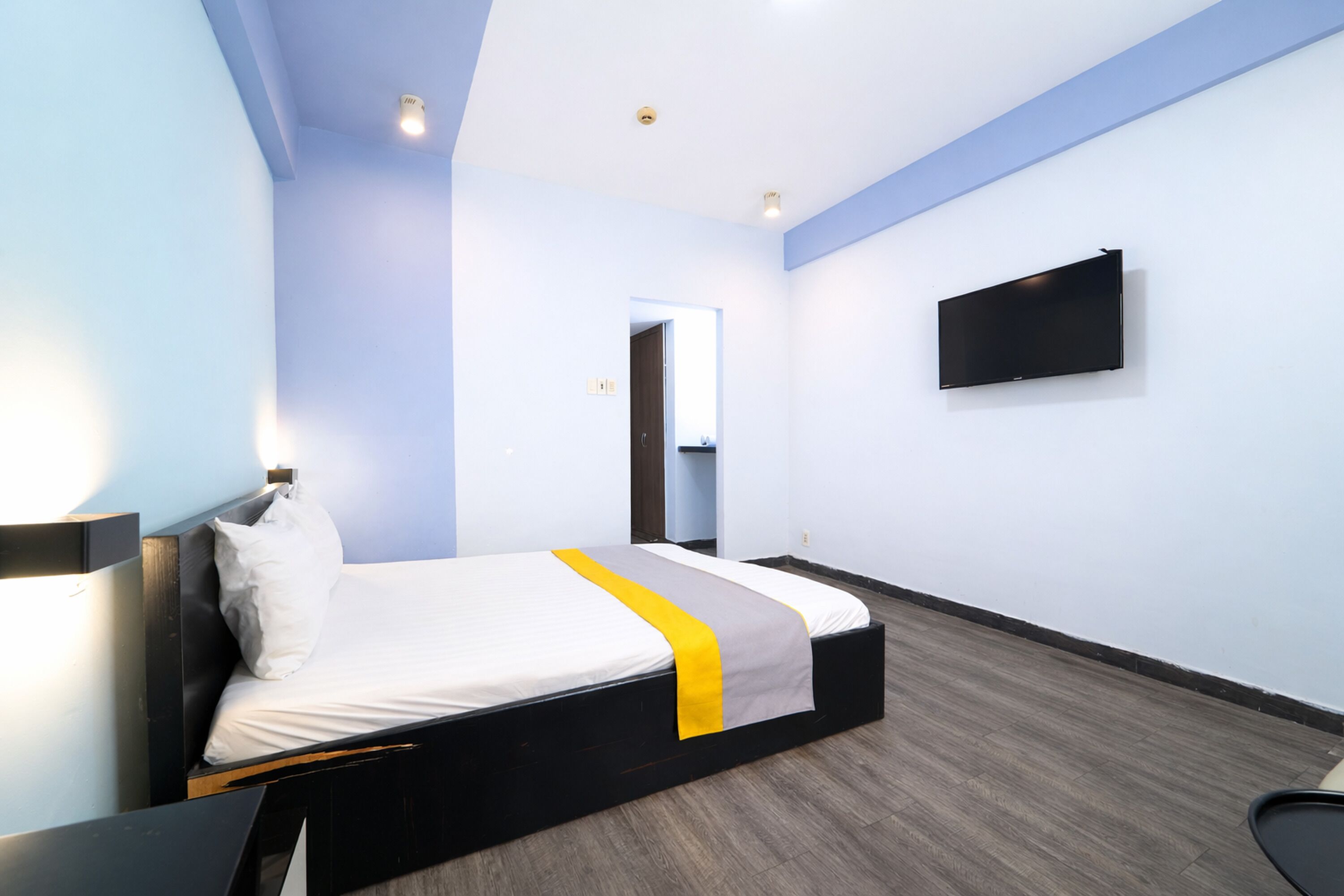 Habitación de hotel con cama, televisor de pantalla plana en la pared y una puerta que da a otra habitación.