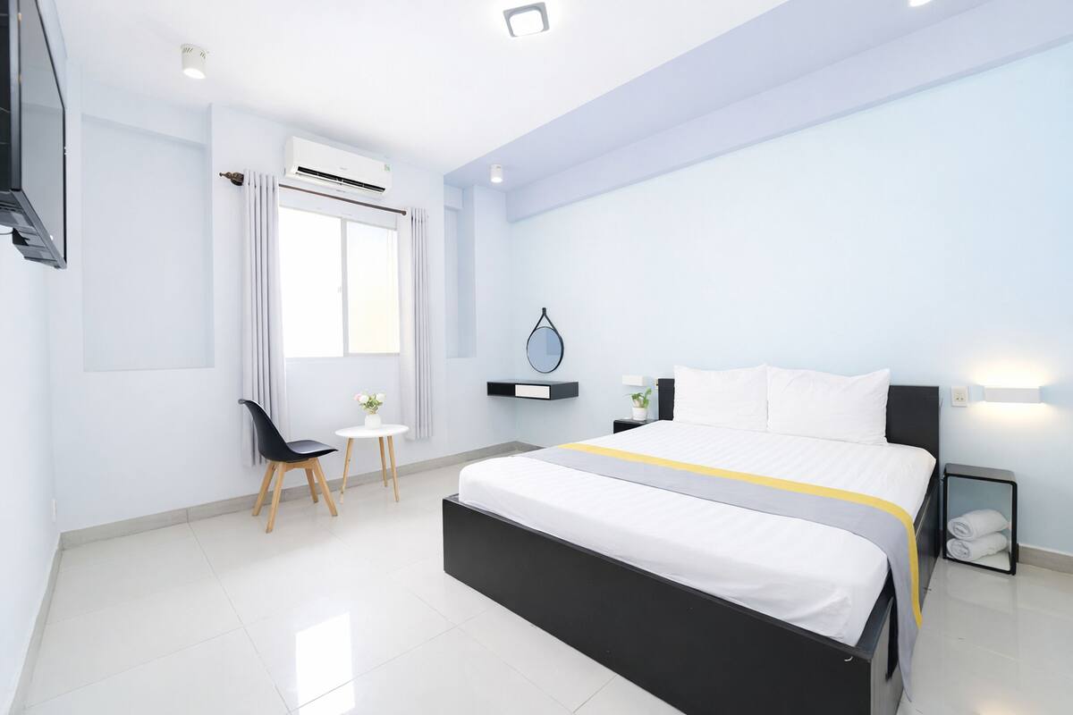 A modern hotel room with a large bed, a small desk, and a window with curtains.