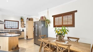 A modern kitchen with a central island, wooden dining table, and chairs. - Burleigh Coastal Escape 4BR Home (Burleigh Heads)